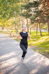 A girl in a black sports uniform is jogging in the evening park. Self-sports concept.