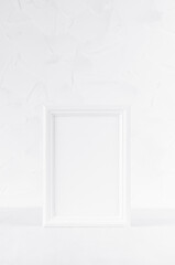 Elegant white empty rectangle photo frame standing on white wood table in simplicity delicate modern minimal soft light interior, vertical. Mockup for presentation, portfolio, text, design, message.