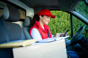 Female courier checking parcels on digital tablet before delivery. - obrazy, fototapety, plakaty