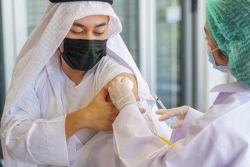Portrait of Arab Muslim man looking at while getting covid vaccine in clinic or hospital, with hand...