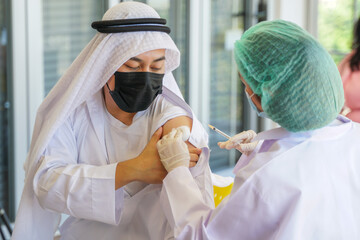 Portrait of Arab Muslim man looking at while getting covid vaccine in clinic or hospital, with hand...