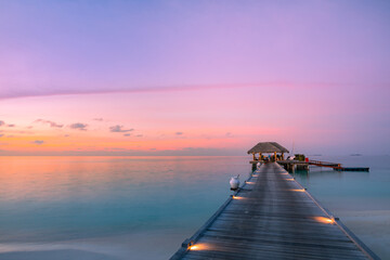 Sunset on Maldives island, luxury water villas resort hotel and wooden pier. Colorful sky and clouds and beach background for summer vacation holiday, traveling destination. Paradise sunset landscape