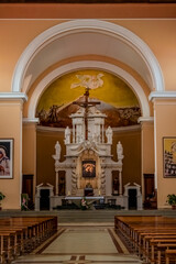 Fototapeta premium Shkoder, Albania - June 21, 2021: Interior of St. Stephen's Catholic Church in Shkoder, vertical. Temple hall with wooden benches against the background of the altar with a crucifix