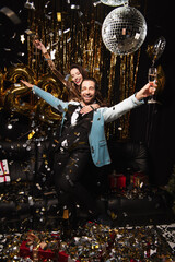 excited couple with champagne glasses in outstretched hands near shiny decoration on black
