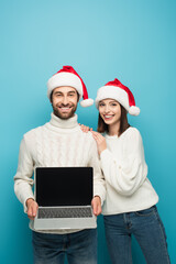 happy man in santa hat holding laptop with blank screen near smiling woman isolated on blue