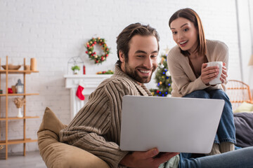 amazed couple looking at laptop in living room with christmas decoration