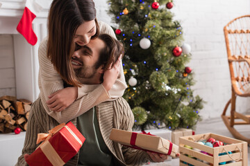 woman embracing happy husband holding christmas presents in living room
