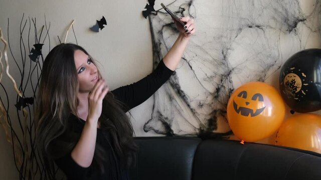 A young brunette woman at a Halloween themed party takes a photo on her smartphone (selfie). Gadgets, smartphone