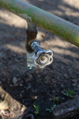 An old water faucet on a green metal pipe. The tap is vertical.