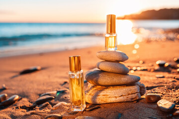Two transparent glass perfume bottles with a golden lid on a sandy beach. Close-up. Sunset in the...
