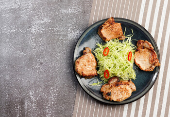 Pork loin chops with cabbage slaw on a round plate on a dark background. Top view, flat lay