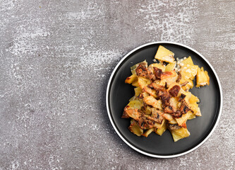 Potato casserole with mushrooms and cheese on a round plate on a dark background. Top view, flat lay