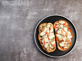 Open faced sandwiches with chicken, pickles and cheese on a round plate on a dark background. Top view, flat lay