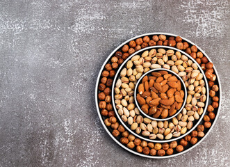 Assortment of various nuts in on a round plate on a dark background. Top view, flat lay