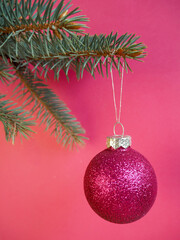 A shiny rain pink Christmas toy on a pink background is hanging on the Christmas tree . side view 