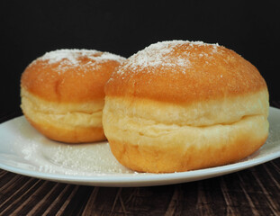two doughnuts sprinkled with powdered sugar lie on a plate on a dark background 