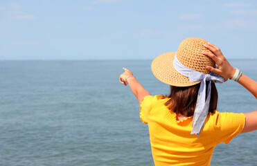 young girl with a straw hat pointing to a bottom point on the horizon on the sea