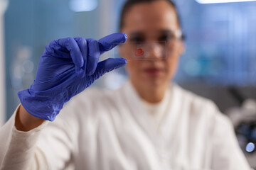 Naklejka premium Chemist doctor holding medical slice analyzing blood sample while working at biochemistry experiment in pharmaceutical hospital laboratory. Microbiologist woman developing vaccine against covid19