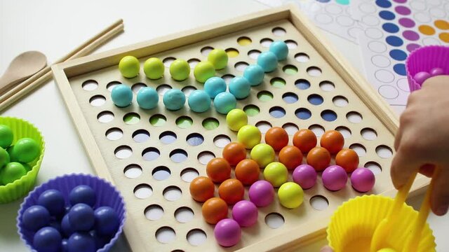 The child lays out colorful balls with tweezers. Wooden toy. Study of colors. Montessori concept, early brain exercise. Early education, fine motoric skills. Kids leisure. Preschool education.
