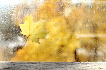 empty table with a linen cape on the background of a blurred window with a maple leaf and drops after the rain front view. a place for autumn mood