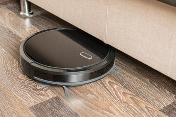 A black robot vacuum cleaner is cleaning the apartment. A portable vacuum cleaner drives into the...