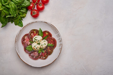 Top view caprese salad with red tomatoes, fresh basil and mozzarella cheese in white plate, copy space