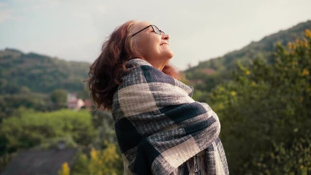 Handheld cinematic shot of a mature adult woman with long hair standing wrapped in a blanket and enjoying the fresh air and a top view at the fall time.