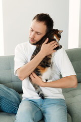 Obraz na płótnie Canvas Upset man hugging beloved cat. Tired unhappy millennial male cuddling with cute pet sit on couch at home. Depressed guy bonding with animal friend. Stress relief, friendship and togetherness concept