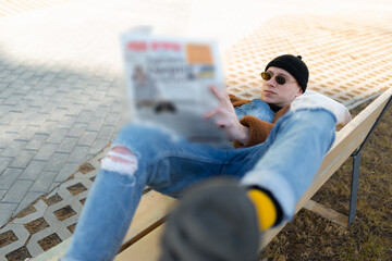 Man wearing casual clothes, reading newspaper, laying down on bench