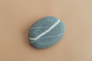 One sea stone of a round form on beige background. Top view of a smooth pebble.