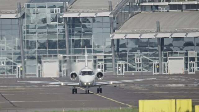 A small plane rides in the background of the airport building. Slow motion video of a private plane traveling to disembark passengers