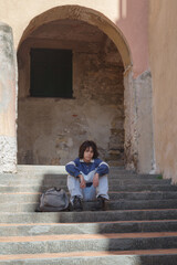 Teenage student with backpack sitting on steps in the street of the Italian old town