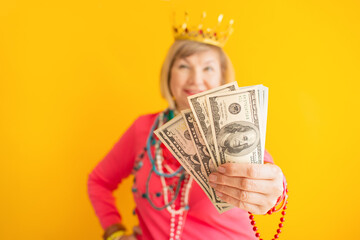 Crazy senior woman with holding money, cashback in stylish clothes on yellow background. Finances and senior people concept