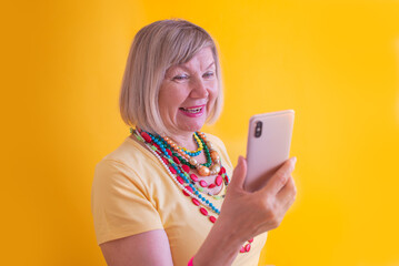 Happy mature elderly senior lady woman talking mobile cell phone in stylish clothes on yellow background