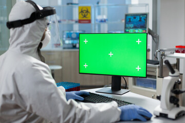 Biologist man with protection ppe medical suit looking at mock up green screen chroma key computer with isolated display while working in biochemistry hospital laboratory. Covid19 vaccine development