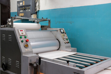Industrial laminator, lamination of paper products. The manufacture of packaging. Outdated equipment. Company. Place for text. - obrazy, fototapety, plakaty
