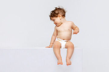 Portrait of little cute toddler boy, baby in diaper joyfully sitting and laughing isolated over...