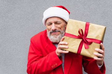 happy mature man in santa hat holding wrapped present near grey wall