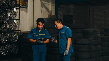 Fototapeta na wymiar Two professional car mechanic using paperwork makes the oil and engine check to the car on lifted automobile at repair service station at night. Skillful Asian guy in uniform fixing car. Car service.