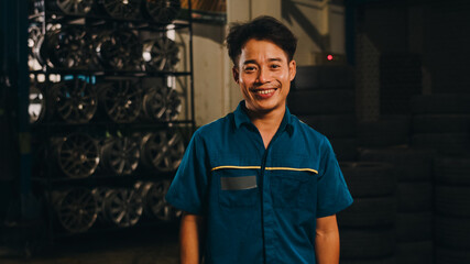 Professional car mechanic looking at camera and smiling at repair service station. Skillful Asian...