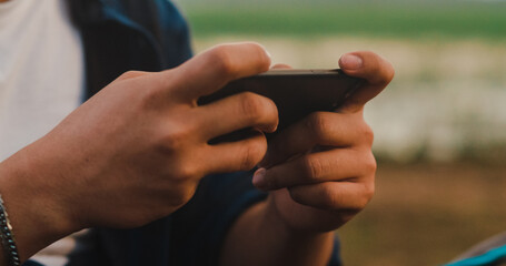 Young asia campers guy use mobile technology phone with internet connection near seaside. Male traveler having fun on summer day at campsite. Outdoor activity, adventure travel, or holiday vacation.
