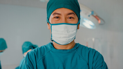 Fototapeta na wymiar Young Asian assistants man looking at camera and smiling after performing invasive surgery on patient in hospital operating room. Diverse team of professional surgeon, Healthcare and medical concept.