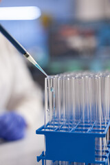 Closeup of chemist researcher dropping solution in transparent test tubes working at vaccine development during microbiological experiment. Microbiology laboratory with medical equipment