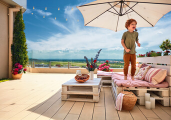 smiling kid having fun, jumping on lounge area made of wooden pallets, summer rooftop patio