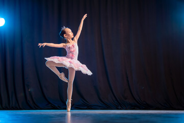 little girl ballerina is dancing on stage in white tutu on pointe shoes classic variation.