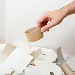 Woman hand tosses a sleeve of adhesive tape into a container for separate collection of paper garbage. Human hand holds cardboard. Paper stuff for recycle. Zero waste concept. Recyclable paper waste