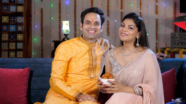 Indian couple wishing their guests a Happy Diwali with a bowl of sweets. A married couple enjoying together at home - Indian festival  festive season  an auspicious occasion  celebration time  fami...