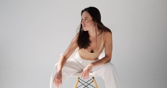 Beautiful young woman looking away while posing sitting on chair over white background