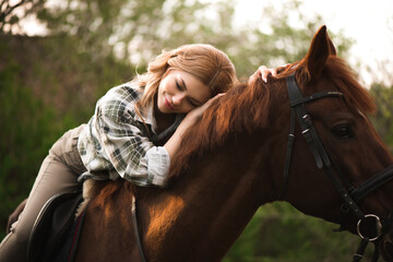 Woman with long hair posing with a brown horse in a forest in a sunny meadow.