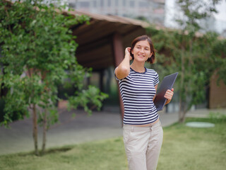 young pretty asian woman walking with laptop in modern park street on remote IT work, summer style casual smiling